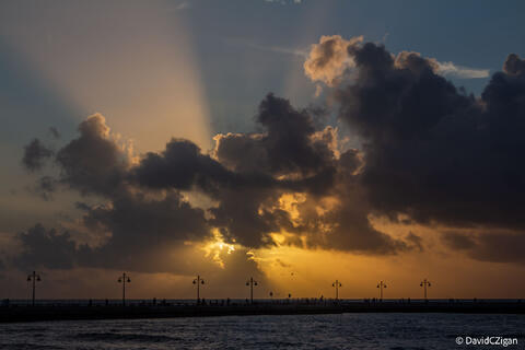 sun rays emerge from behind clouds over the water near sunrise