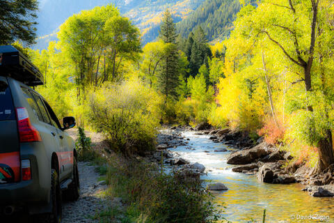 colorful pointillism-style image of stream flowing in a mountain valley in the autumn with a 4x4 vehicle on a road