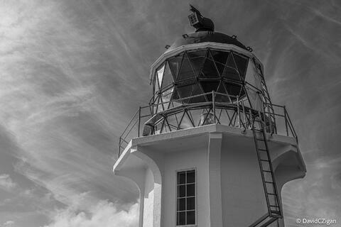 black and white close-up view of a lighthouse with wispy clouds overhead