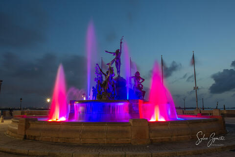 colorful lights illuminate a water fountain with sculptures after sunset