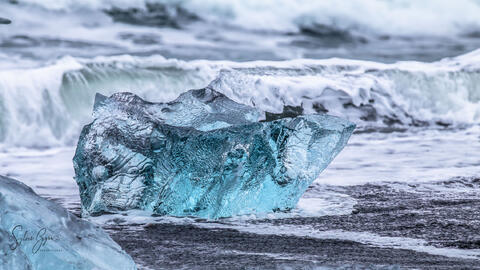 translucent blue ice on a beach with waves behind it