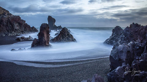 long exposure of water receding from a rocky black beach