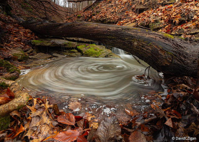 long-exposure of a swirling pool of water under a fallen tree log in a wooded valley in the autumn