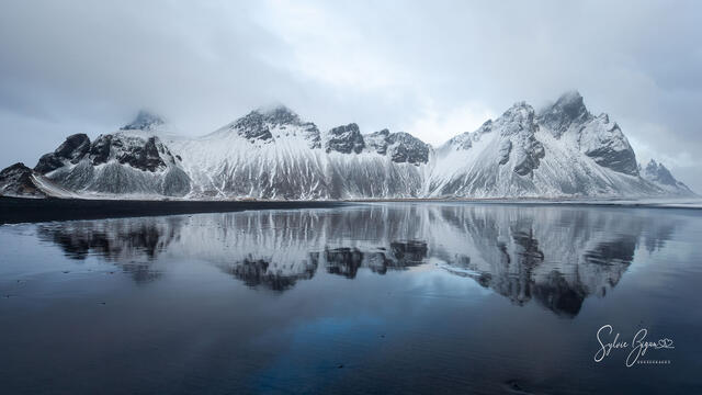 panoramic winter scene of snow-covered mountains on a wet beach